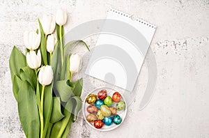 Top view of white tulips, blank calendar and colored easter eggs on concrete backgrund with copy space