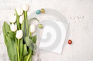 Top view of white tulips, blank calendar and colored easter eggs on concrete backgrund with copy space