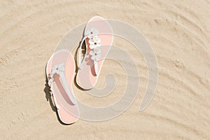 Top view of white woman flip flops with flowers on sandy beach. Summer vacation concept on a sunny day