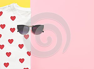 Top view of white woman t-shirt with sunglasses on pink and yellow background