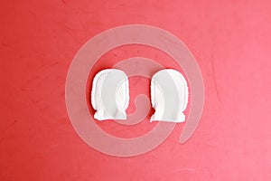 Top view of white wool baby mittens on a red background