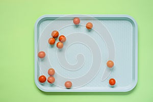 Top view of whole cherry tomatoes on a tray on green background