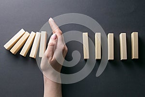 Top view whomen hand stopping falling dominos in a business crisis management conceptual image