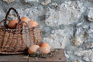 Top view of wicker basket with farm eggs and three eggs on hay and wooden table