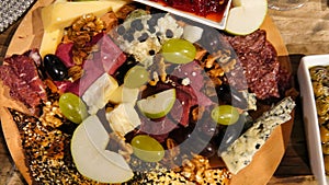 Top view of wine appetizers; cheese, salami, sausage, dried meat, olives, grapes, bread, red sweet pepper sauce, sliced apples, em