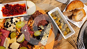 Top view of wine appetizers; cheese, salami, sausage, dried meat, olives, grapes, bread, red sweet pepper sauce, sliced apples, em