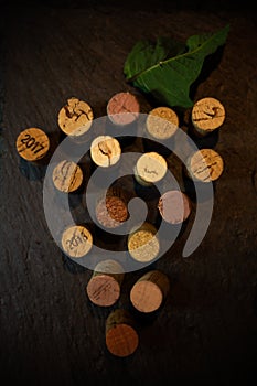 Top view wine corks placed forming a bunch of grapes with a grape leaf over a slate with dark background