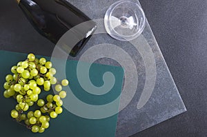 Top view of wine glass, bottle of wine and ripe grapes on the grey dark surface
