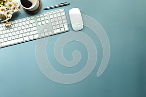 Top view, wireless keyboard, mouse and coffee cup on blue background with copy space