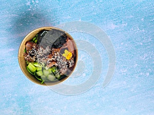 Top view of wok box, bowl of rice on black background. Rice fried and stirred with salmon, avocado, onion, mushrooms, broccoli