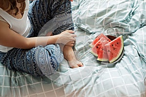 Top view of woman in blue pajamas on the bed eating a watermelo