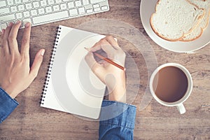 Top view of woman business hand writing  the notebook and using computer on desk and have coffee, toast on the wooden table