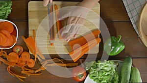Top view of woman chief making salad healthy food and chopping carrot on cutting board in the kitchen