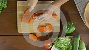 Top view of woman chief making salad healthy food and chopping carrot on cutting board in the kitchen