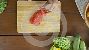 Top view of woman chief making salad healthy food and chopping tomato on cutting board in the kitchen