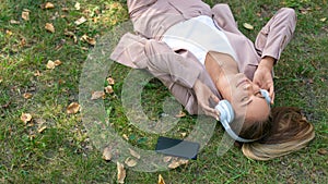 Top view of a woman enjoying the music while lyuing on the grass in city park.