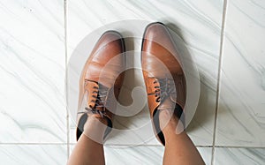 Top view woman feet wearing oversize brown men leather shoes