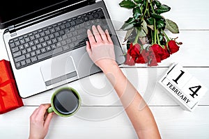 Top view of woman hand holding cup of coffee and working on open laptop computer, copy space. Valentines day background.