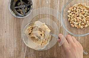 Top view of woman hand holding knife with homemade peanut butter made in grinder on the wooden background