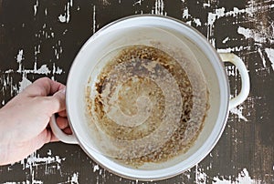 Top view of woman hand holding pan with burnt bottom after cooking porridge on the brown background