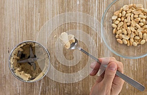 Top view of woman hand holding spoon with homemade peanut butter made in grinder on the wooden background