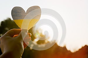 Top view of woman hand holding Ukraine flag painted heart against orange sunset sky. Concept symbol of help, support and stop war