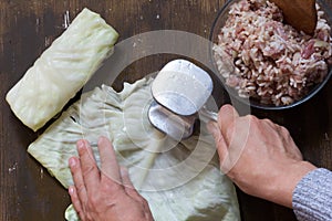 Top view of woman hands beating cabbage leaf with meat tenderiser before stuffing on brown background