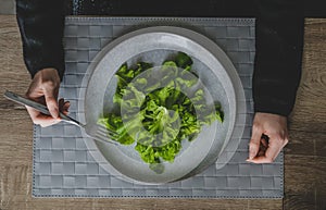 Top view of woman hands and big grey plate with green leaves of salad.