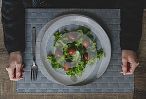 Top view of woman hands and big grey plate with green leaves of salad.