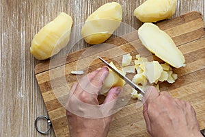 Top view of woman hands cutting scrubbed boiled potatoes in jackets using knife on the wooden background