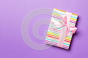 Top view woman hands holding Christmas present box with pink bow on purple background with copy space