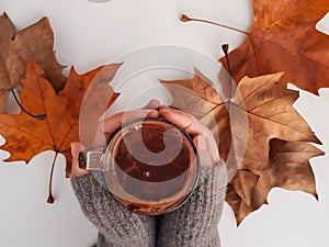 Top view of woman hands holding a cup of hot chocolate with fallen autumn leaves on table