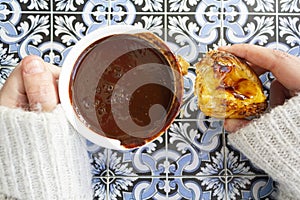 Top view of woman hands holding cup with hot chocolate and portuguese custard tart called pastel de nata on portuguese tiles photo