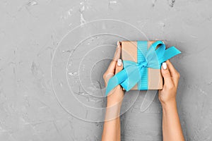 Top view woman hands holding present box with blue bow on gray background with copy space