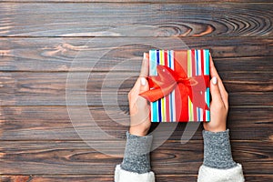 Top view woman hands holding present box with colored bow on dark wooden background with copy space