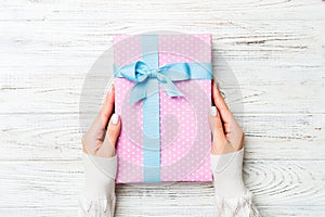 Top view woman hands holding present box with colored bow on white rustic wooden background with copy space