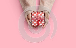 Top view of Woman hands is holding a small red gift box over pink  background