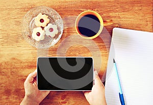 Top view of woman hands holding tablet device with empty screen, with cookies and coffee cup. image is retro filtered.