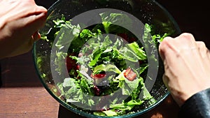 top view woman hands making greek green salad, stirring with forks, closeup salad bowl