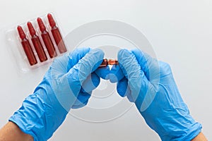 Top view of woman hands in medical glove opening ampoule with vitamin group B for injection on the white background