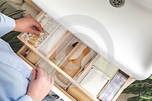 Top view of woman hands neatly organizing bathroom amenities and toiletries in drawer in bathroom.