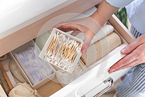 Top view of woman hands neatly organizing bathroom amenities and toiletries in drawer in bathroom.