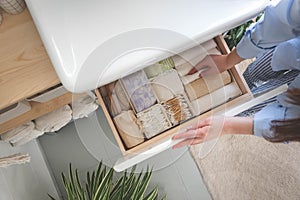 Top view of woman hands neatly organizing bathroom amenities and toiletries in drawer in bathroom.