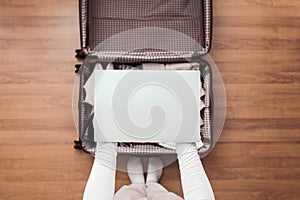 Top view of woman hands packing laptop in luggage suitcase for a new journey.