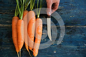 Top view of woman hands peeling fresh raw carots on rustic blue table