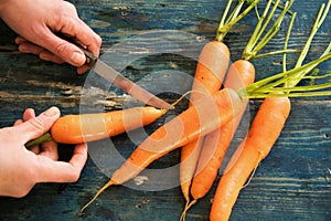 Top view of woman hands peeling fresh raw carots on rustic blue table