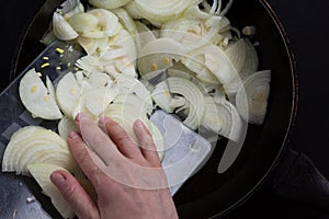 Top view of woman hands putting cut onion into pan to fry or caramelize on the black background