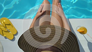 Top view of woman in hat playing with water near pool, enjoying weekend
