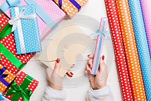 Top view of a woman holding an envelope in one hand and a small present in another on wooden background. New Year decorations.