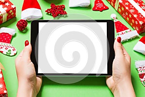 Top view of woman holding tablet in her hands on green background made of Christmas decorations. New Year holiday concept. Mockup